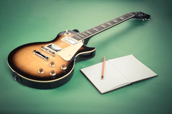 Electric guitar with notepad and old camera on green background