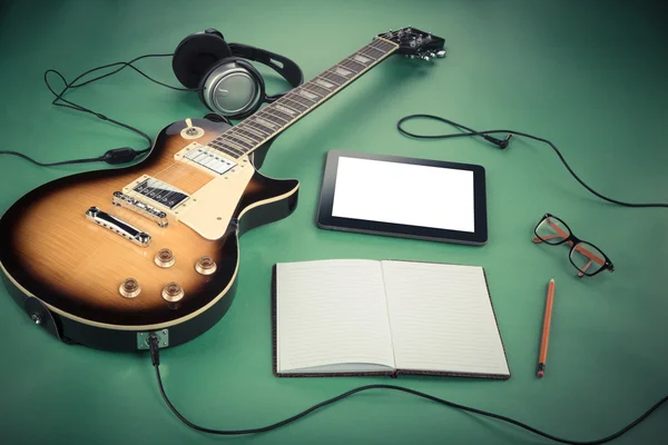 Electric guitar with notepad and old camera on green background