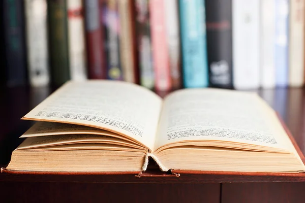 Open book on the wooden table with defocused books in the background