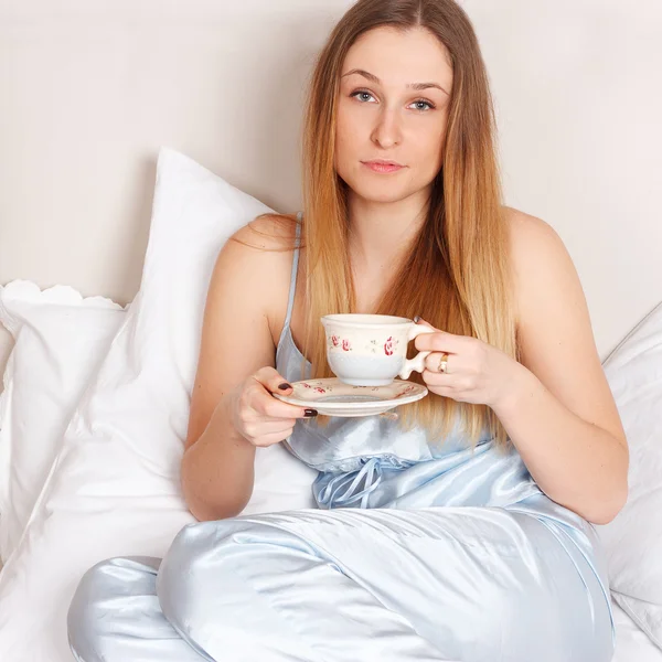 Woman in pajamas holding cup of tea on bed