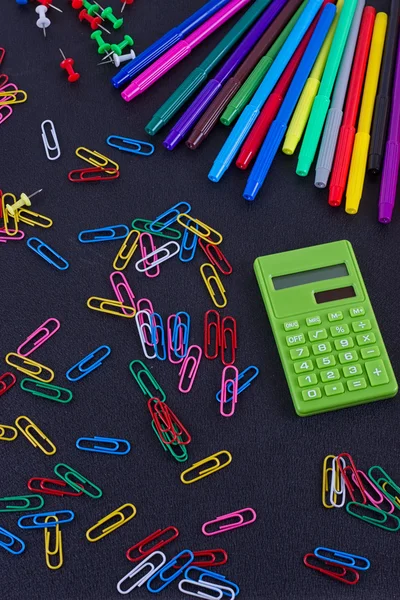 Calculator, paper clips, markers on black Board