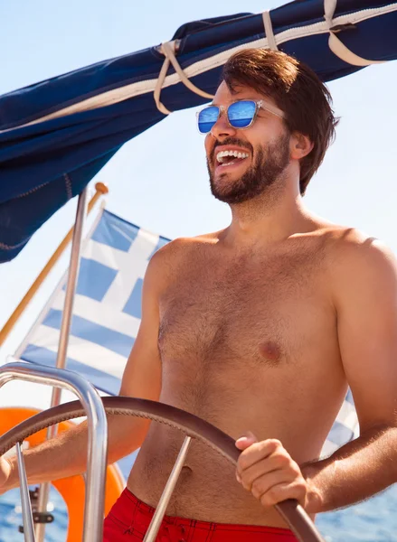 Happy guy behind wheel of sailboat
