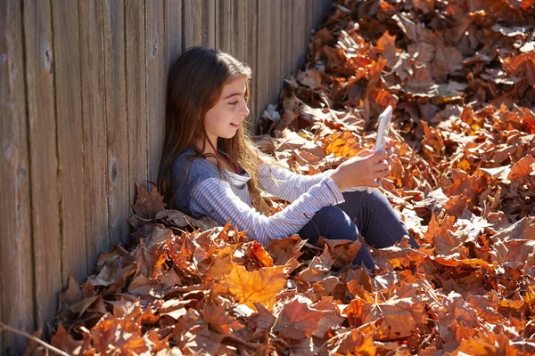 Kid girl playing tablet pc in autumn leaves