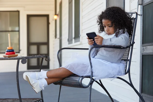 Kid girl sitting in the porch playing smartphone