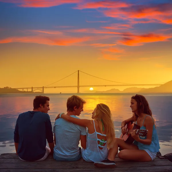 Friends group playing guitar in sunset pier at dusk