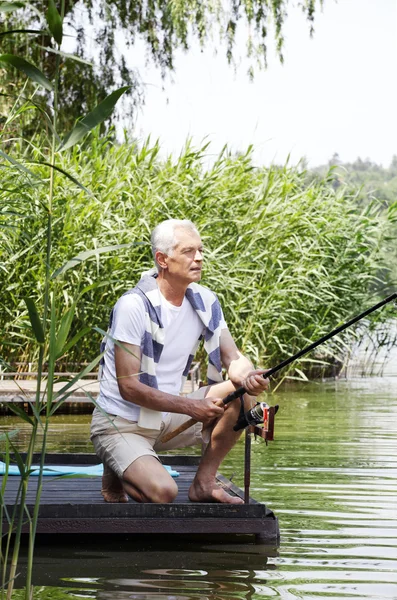 Senior man  at the lakeside and fishing.