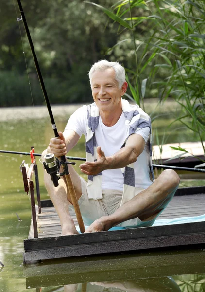 Senior man sitting at pier and fishing.
