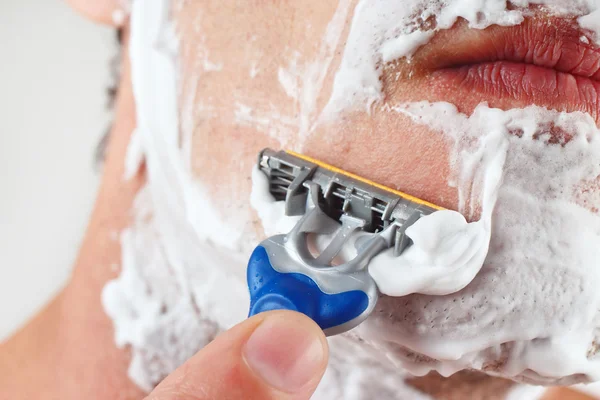 Hand man with a disposable razor shaving his face closeup