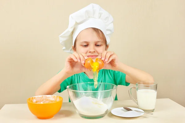 Little boy in chef hat pours egg for baking cake