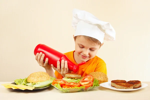 Little funny chef puts ketchup on hamburger