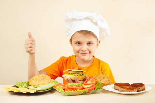 Little boy in chefs hat shows how to cook hamburger
