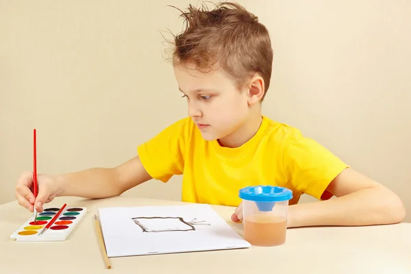 Young artist in yellow shirt painting with watercolors
