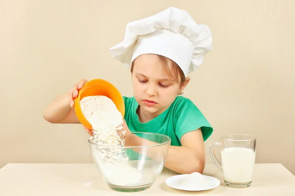 Young boy in chefs hat pours flour for baking cake