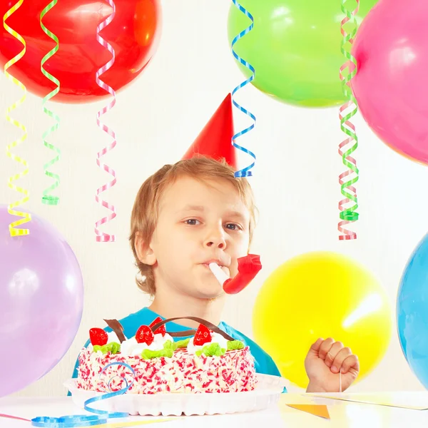 Little boy in festive hat with birthday cake with whistle and holiday balloons