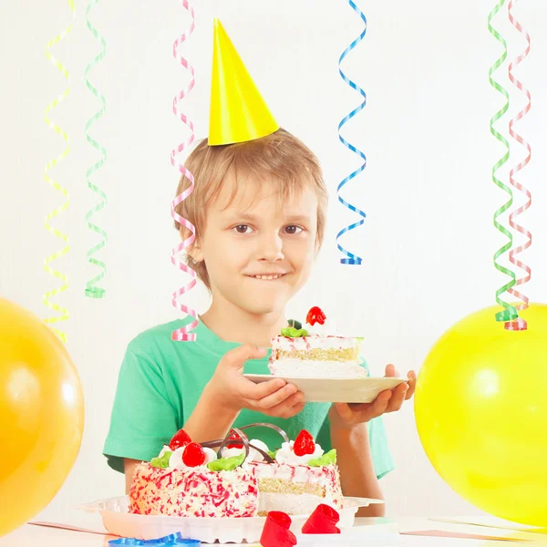 Little kid in holiday hat with piece of birthday cake and balloons