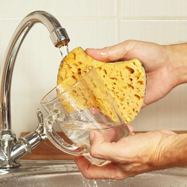 Hands wash the glass under running water in kitchen