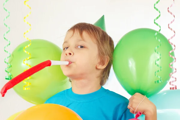 Little boy in festive hat with whistle and holiday balloons and streamer