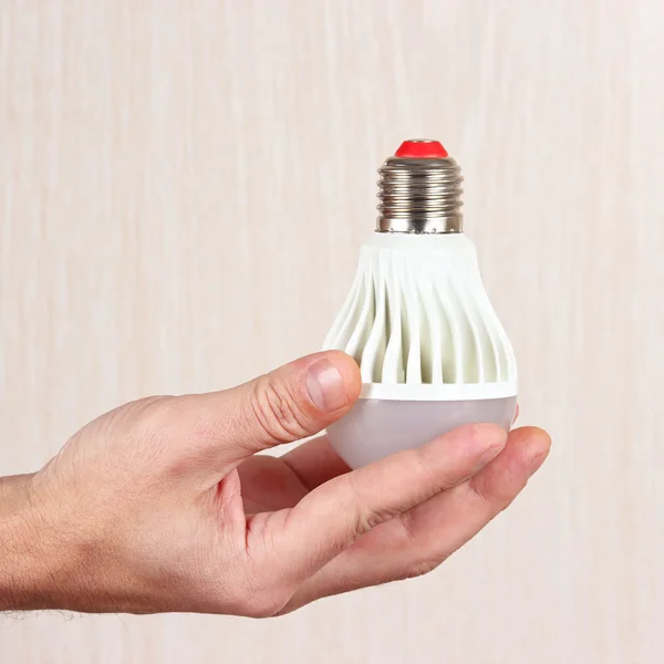 Hand holding a light bulb on light wood background