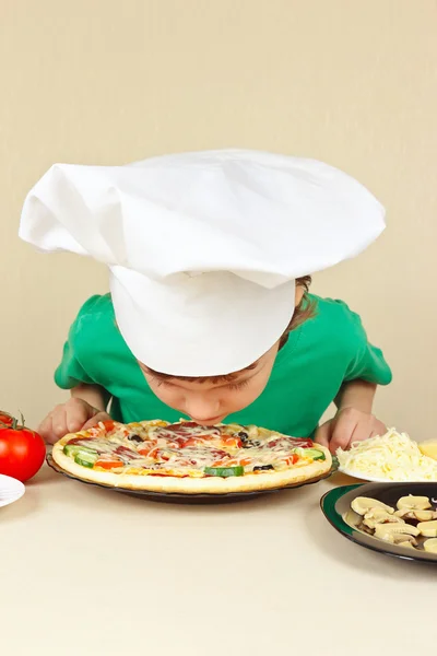 Little funny chef sniffing aroma of cooked pizza