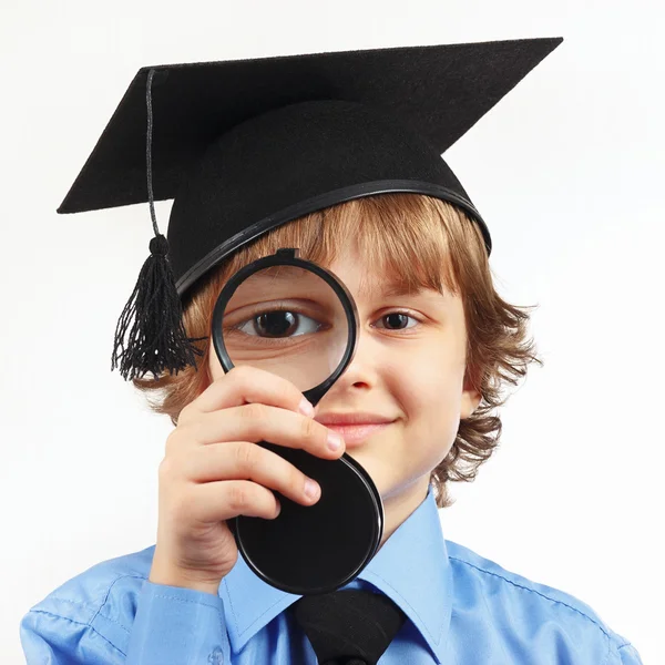 Little boy in academic hat with a magnifying glass on white background