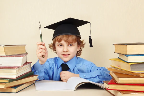 Little boy in academic hat with rarity pen among old books