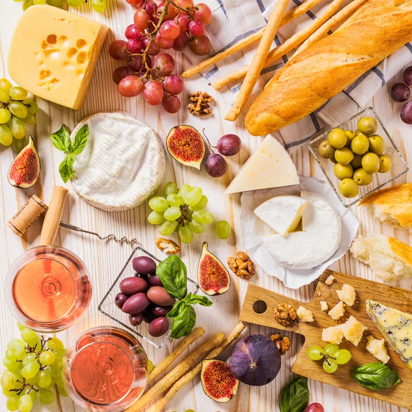 Assortment of cheeses, fruits, breads, wine and snacks on white