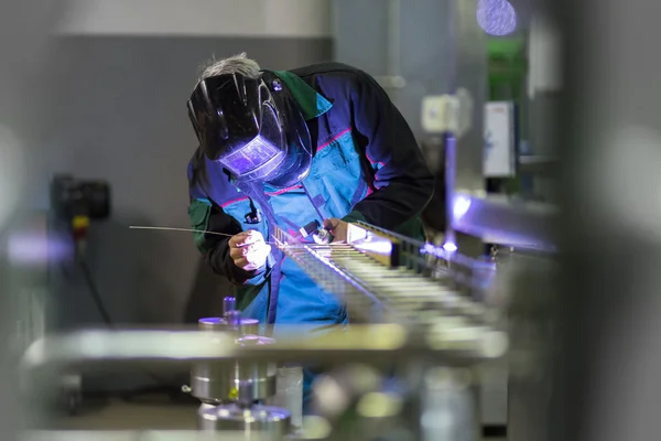 Industrial worker welding in metal factory.