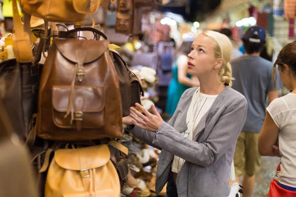 Casual blond woman shopping for leather bag.