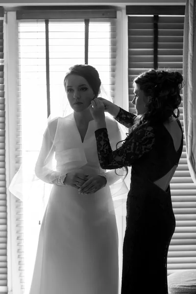 Black and white portrait of bridesmaid helping bride in preparat