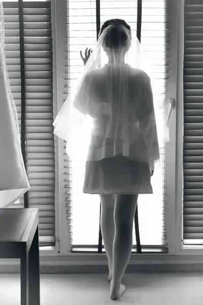 Black and white photo of sexy bride looking out of window