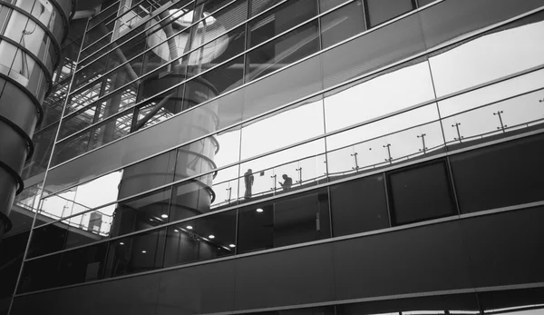 Black and white shot of people reflecting in modern glass buildi