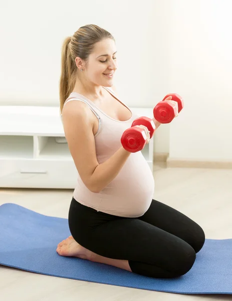 Expectant mother exercising with dumbbells on fitness mat