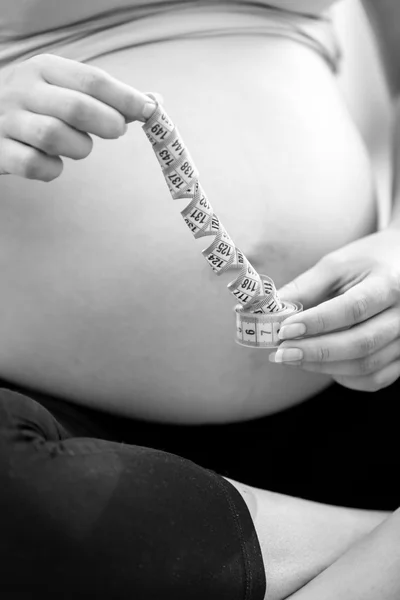 Black and white photo of pregnant woman posing with measuring ta