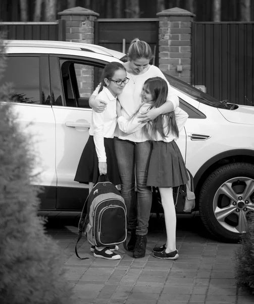 Black and white photo of mother hugging daughters after school