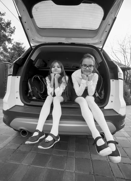 Black and white photo of two schoolgirls sitting in open car tru