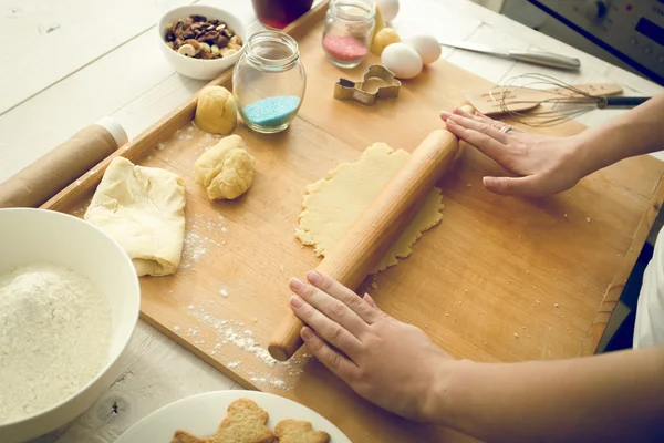 Toned photo of woman rolling dough on wooden board