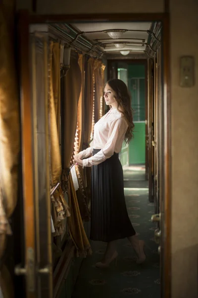 Young woman standing at old train and looking out of window