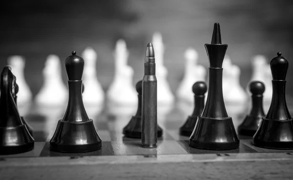 Black and white closeup shot of bullet in row of chess pieces