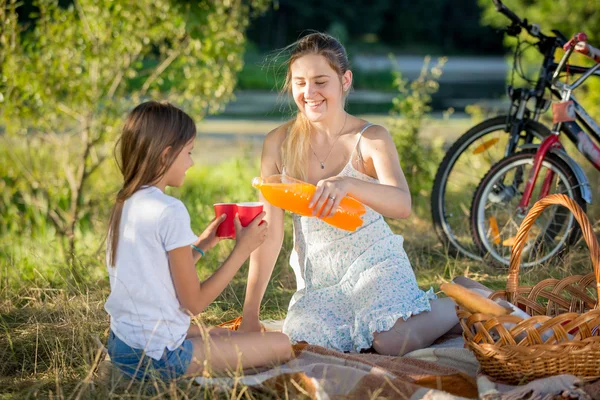 Portrait of mother pouring juice from bottle into daughter's cup