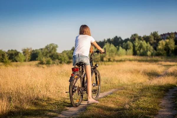 Girl in shorts and t-shirt cycling in meadow at sunset