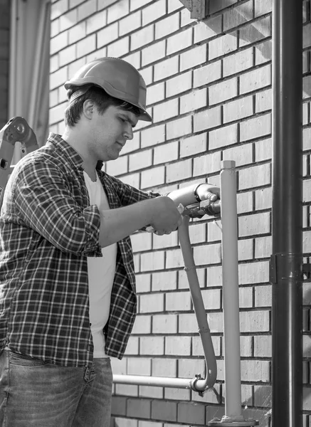 Black and white portrait of plumber assembling pipes on outer wa