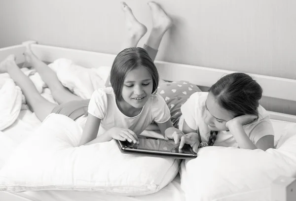 Black and white portrait of two sisters using tablet on bed at m