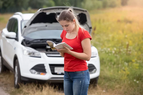 Portrait of stressed woman standing at broken car and reading ow