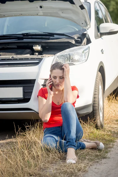 Stressed woman sitting at the broken car on roadside and talking