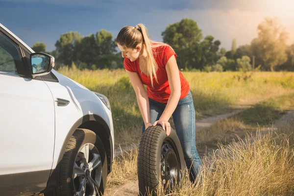 Beautiful woman rolling spare tire to change the flat one