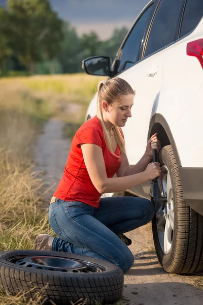 Beautiful woman changing flat tire on the rural road