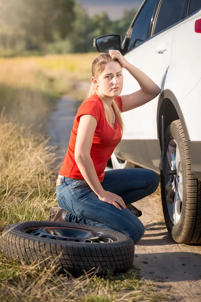 Woman sitting at broken car and trying to change flat tire