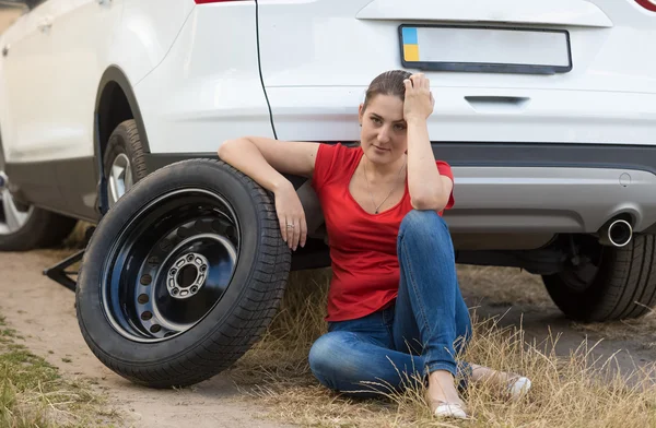 Upset woman sitting on ground next to the spare tire