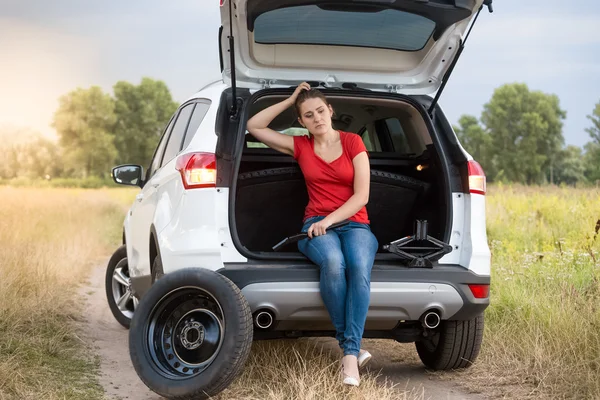 Sad woman sitting in open trunk of broken car on the rural road