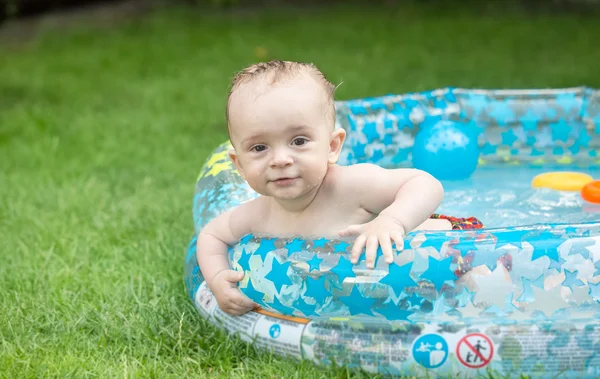 Adorable baby boy swimming in the inflatable swimming pool at ga